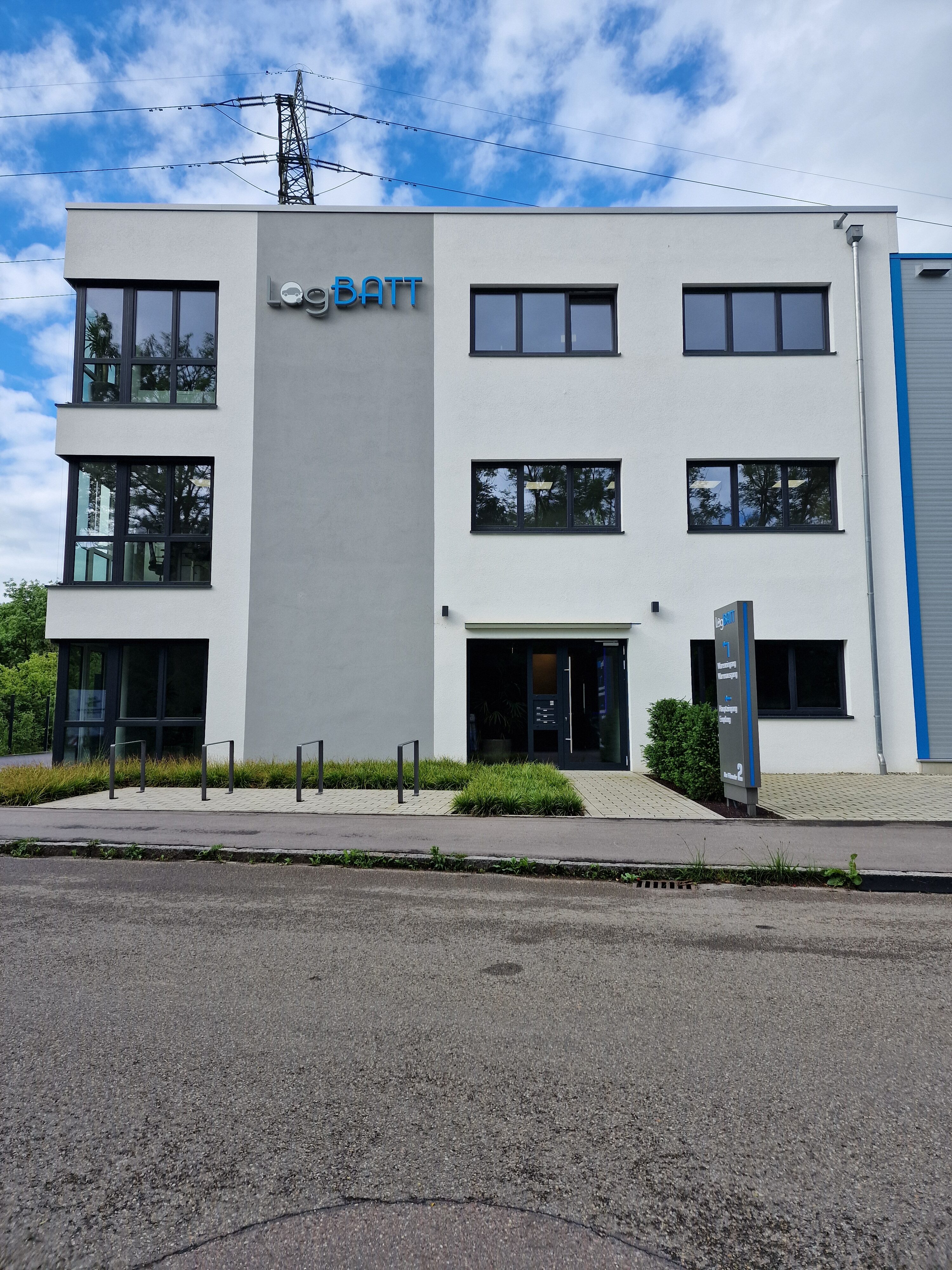 Ein modernes Bürogebäude mit weißer Fassade und großen Fenstern an einem bewölkten Tag.